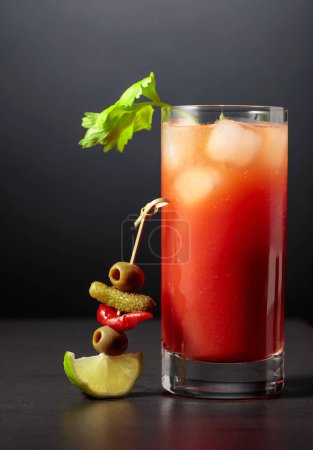 Téléchargez les photos : Cocktail Bloody Mary avec céleri, cornichon, olive, citron vert et poivron rouge. Boisson tomate sur fond noir. - en image libre de droit