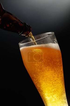 Photo for Pouring beer from a bottle into a tall glass. - Royalty Free Image