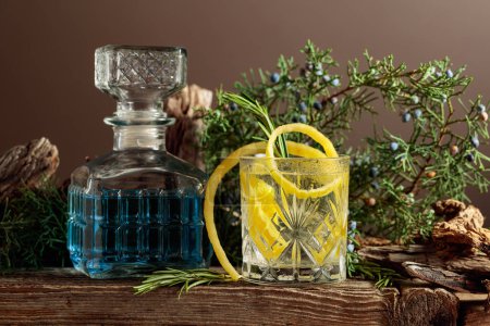 Téléchargez les photos : Cocktail gin-tonic avec glace, citron et romarin dans un verre congelé. Une boisson rafraîchissante avec des branches de genièvre et des chicots sur une vieille planche. - en image libre de droit