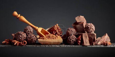 Photo for Chocolate truffles with broken pieces of black chocolate and cocoa powder. Chocolate, cinnamon sticks and anise on a dark background. Copy space. - Royalty Free Image