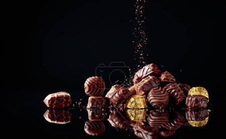 Téléchargez les photos : Divers bonbons au chocolat sur un fond noir saupoudré de pépites de chocolat. Espace de copie. - en image libre de droit