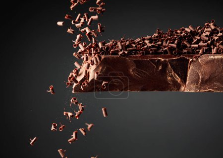 Téléchargez les photos : Grand morceau de chocolat noir et miettes de chocolat tombant sur un fond noir. - en image libre de droit
