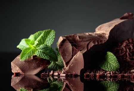 Téléchargez les photos : Morceaux de chocolat noir amer et pépites de chocolat avec menthe sur un fond réfléchissant noir. Espace de copie. - en image libre de droit