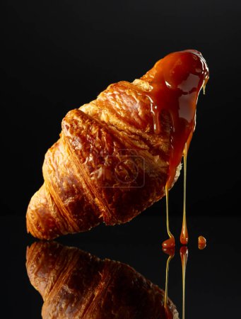Photo for Fresh baked croissant with caramel sauce on a black reflective background. - Royalty Free Image