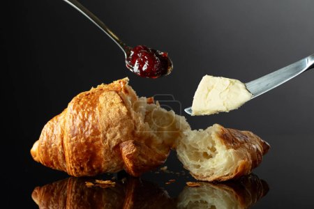 Foto de Croissant recién horneado con mermelada de frambuesa y mantequilla sobre un fondo negro reflectante. - Imagen libre de derechos
