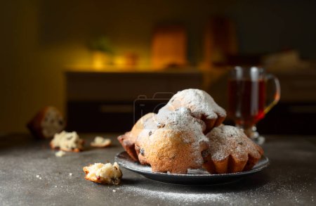 Foto de Magdalenas de pasas caseras espolvoreadas con azúcar en polvo. Desayuno en la mesa de la cocina. - Imagen libre de derechos