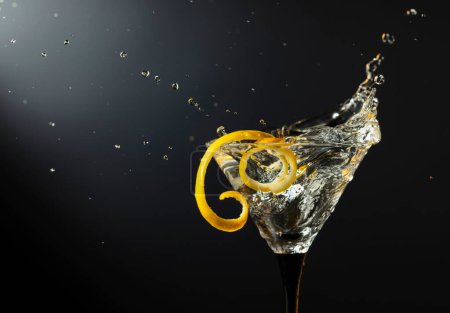 Photo for Glass of classic dry martini cocktail with lemon peel on a black background. Martini with splashes. Free space for your text. - Royalty Free Image