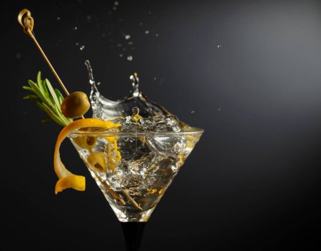 Téléchargez les photos : Cocktail martini sec classique aux olives vertes, écorce de citron et romarin sur fond noir. Martini aux éclaboussures. Espace libre pour votre texte. - en image libre de droit