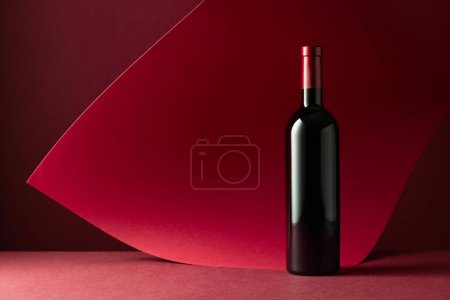 Téléchargez les photos : Bouteille de vin rouge sur fond rouge. Copiez l'espace pour votre texte. - en image libre de droit