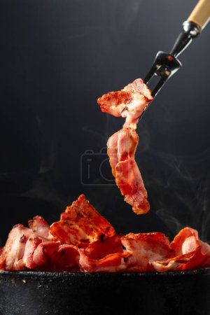 Photo for Fried steaming bacon slices on a black background. Copy space. - Royalty Free Image