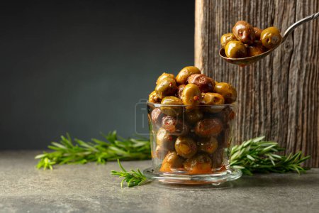 Téléchargez les photos : Olives épicées dans un bol en verre. Bol avec olives conservées et brindilles de romarin sur une table en pierre. - en image libre de droit