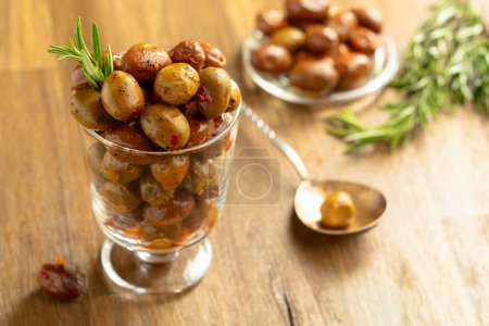 Photo for Spicy olives in a glass bowl. Bowl with preserved olives and rosemary twigs on a wooden table. - Royalty Free Image