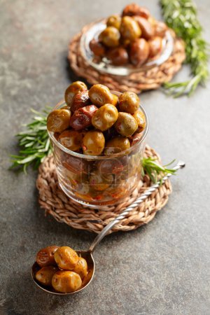 Photo for Spicy olives in a glass bowl. Bowl with preserved olives and rosemary twigs on a stone table. - Royalty Free Image