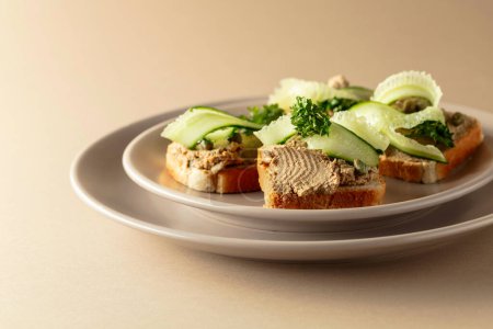 Téléchargez les photos : Sandwichs ouverts avec pâté, concombre frais, câpres et persil. Toasts avec pâté sur fond beige. - en image libre de droit