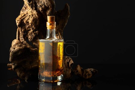 Photo for Olive oil with pepper, bay leaf, coriander, and thyme. Bottle of spicy oil and olive tree snag on a black background. Copy space. - Royalty Free Image