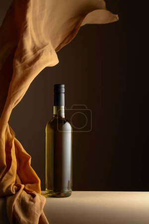 Téléchargez les photos : Bouteille de vin blanc et volutes de tissu beige sur fond sombre. - en image libre de droit