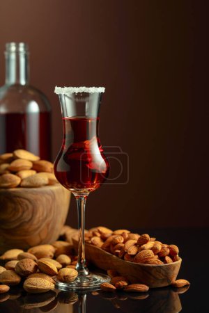 Foto de Licor italiano fuerte y alcohólico Amaretto con almendras y frutos secos sobre un fondo marrón. - Imagen libre de derechos