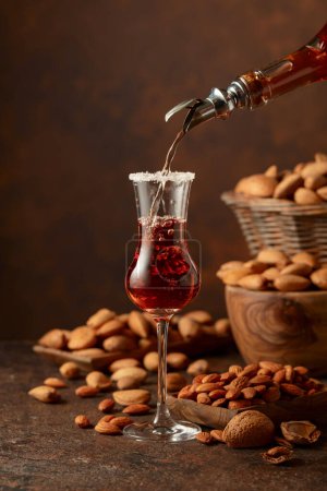 Foto de Licor italiano fuerte y alcohólico Amaretto con almendras y nueces en una mesa de té. - Imagen libre de derechos