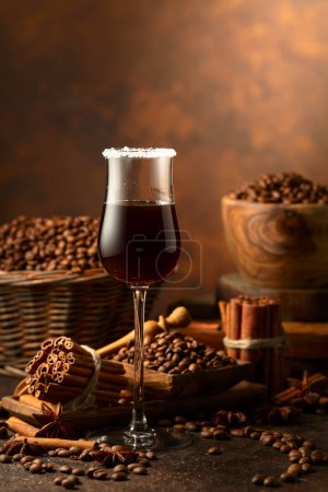 Téléchargez les photos : Liqueur de café sur fond brun. Les grains de café, les bâtonnets de cannelle et l'anis sont éparpillés sur une table vintage. - en image libre de droit