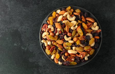 Téléchargez les photos : Mélange de noix séchées et de raisins secs sur un fond de pierre noire. Vue de dessus. Espace de copie. - en image libre de droit