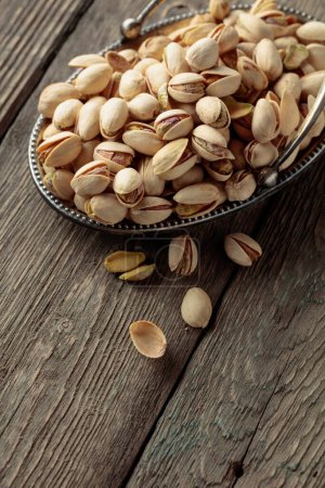 Foto de Salted pistachios in a dish on an old wooden table. - Imagen libre de derechos