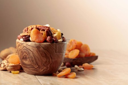 Foto de Frutas secas y frutos secos sobre una mesa de cerámica beige. La mezcla de nueces, albaricoques y pasas en un tazón de madera. - Imagen libre de derechos