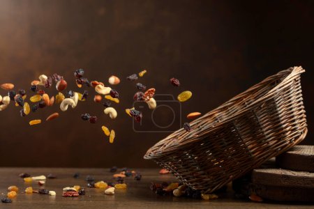 Photo for Dried fruits and nuts fall in basket. The mix of dried nuts and raisins on a brown background. Copy space. - Royalty Free Image