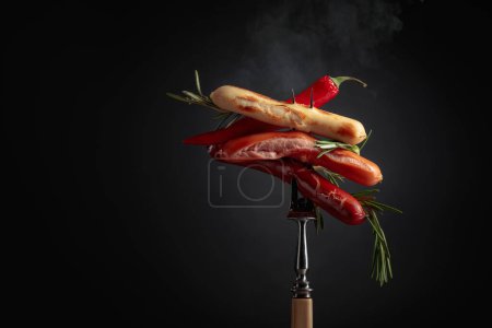 Photo for Various hot sausages with rosemary, and hot pepper on a fopk. Copy space. - Royalty Free Image