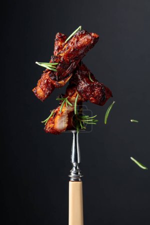 Téléchargez les photos : Ventre de porc grillé avec romarin sur une fourchette. Fond noir. - en image libre de droit