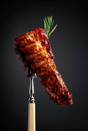 Foto de Costillas de cerdo a la plancha con romero en un tenedor. Fondo negro
. - Imagen libre de derechos