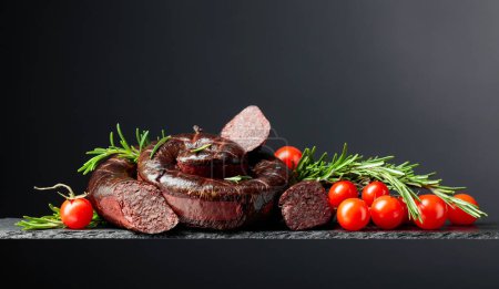 Photo for Traditional European black pudding or blood sausage with rosemary and tomatoes on a black background. Copy space. - Royalty Free Image