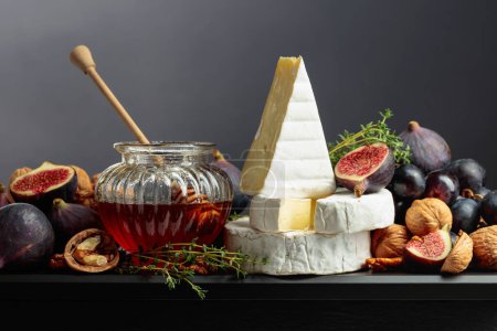 Photo for Camembert cheese with figs, grapes, walnuts, honey, and thyme. Soft cheese with fruits on a black background. - Royalty Free Image