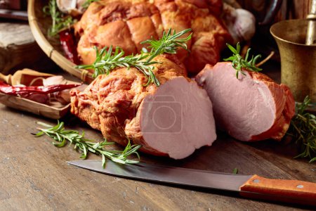 Photo for Smoked ham with herbs, spices, and kitchen utensils on an old wooden table. - Royalty Free Image