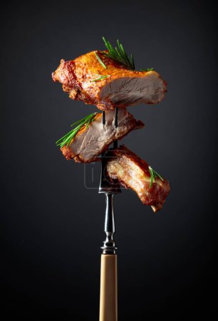 Foto de Costillas de cerdo a la parrilla en un tenedor. Carne asada espolvoreada con romero sobre un fondo negro. - Imagen libre de derechos