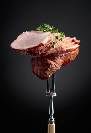Photo for Sliced smoked gammon with thyme branches on a fork. Natural product from an organic farm, produced by traditional methods. - Royalty Free Image