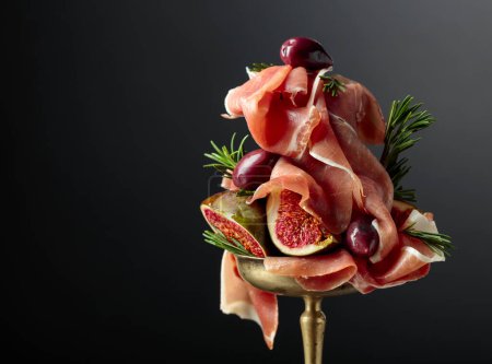 Photo for Prosciutto with figs, rosemary, and red olives in an old brass dish. Copy space. - Royalty Free Image