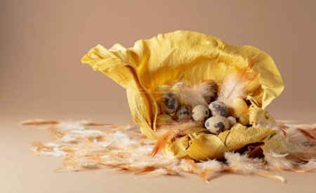 Foto de Nido de papel crepé con huevos de Pascua y plumas sobre un fondo beige. - Imagen libre de derechos