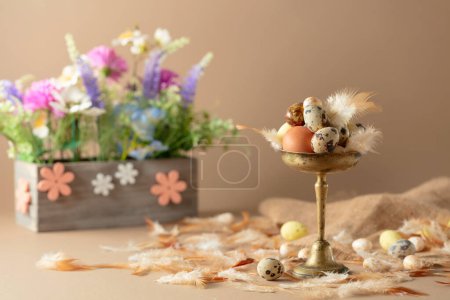 Photo for Easter composition with eggs, feathers, and spring flowers on a beige background. Selective focus. - Royalty Free Image