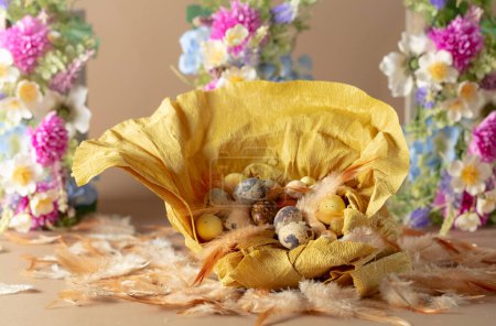 Foto de Nido de papel crepé con huevos de Pascua, plumas y flores de primavera sobre un fondo beige. Concéntrate en un primer plano. - Imagen libre de derechos