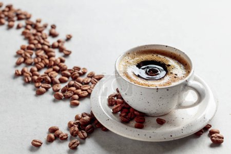 Téléchargez les photos : Café noir et grains de café sur une table en marbre blanc. Une goutte de café tombe dans une tasse. Espace de copie. - en image libre de droit