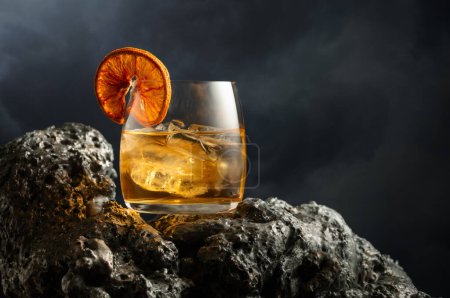 Photo for Old fashioned cocktail with ice and dried orange slice on a grey stone. Cold drink on a  background of cloudy sky. - Royalty Free Image