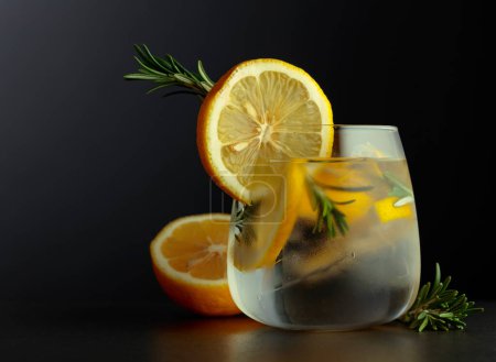 Téléchargez les photos : Cocktail gin-tonic avec tranches de citron et brindilles de romarin sur fond noir. Espace de copie. - en image libre de droit