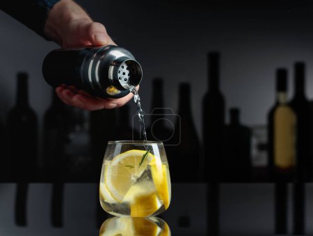 Téléchargez les photos : Cocktail Gin-tonic sur fond noir réfléchissant. Dans les silhouettes de fond de diverses bouteilles. - en image libre de droit