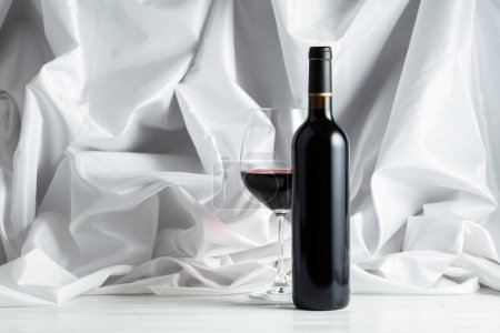 Photo for Red wine on a white wooden tfble. In the background white satin curtain. - Royalty Free Image