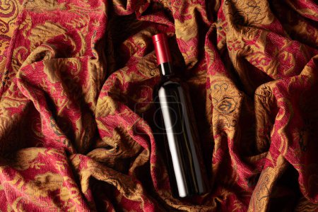 Téléchargez les photos : Bouteille de vin rouge sur une tapisserie rétro à l'ornement floral rouge foncé et doré. Vue du dessus. - en image libre de droit