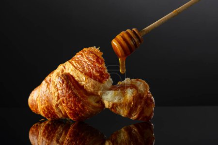 Photo for Fresh baked croissant with honey on a black reflective background. Copy space. - Royalty Free Image
