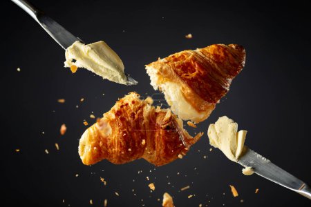 Photo for Fresh baked croissant in air and knifes with butter on a black background. - Royalty Free Image