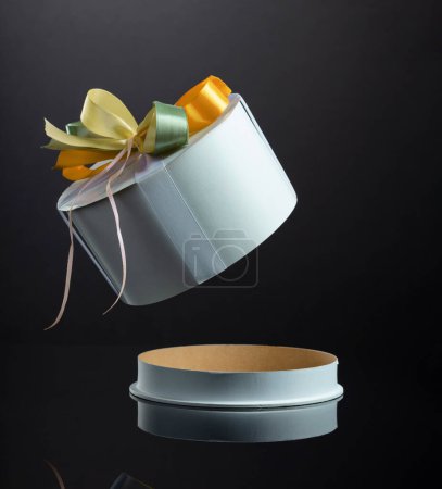 Photo for Rounded white cardboard gift box with colorful ribbons. Opened empty gift box on a black reflective background. - Royalty Free Image