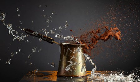 Photo for Black coffee making. Old copper cezve, water splashes, and grounded coffee in motion. - Royalty Free Image
