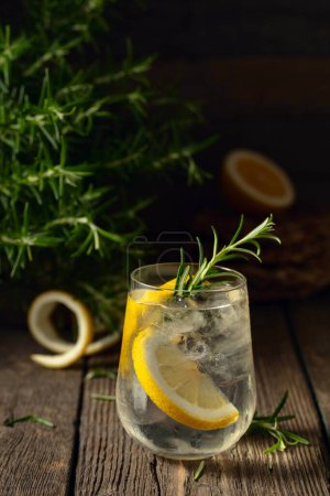 Photo for Cocktail gin tonic with ice, lemon, and rosemary on a old wooden table. Copy space. - Royalty Free Image